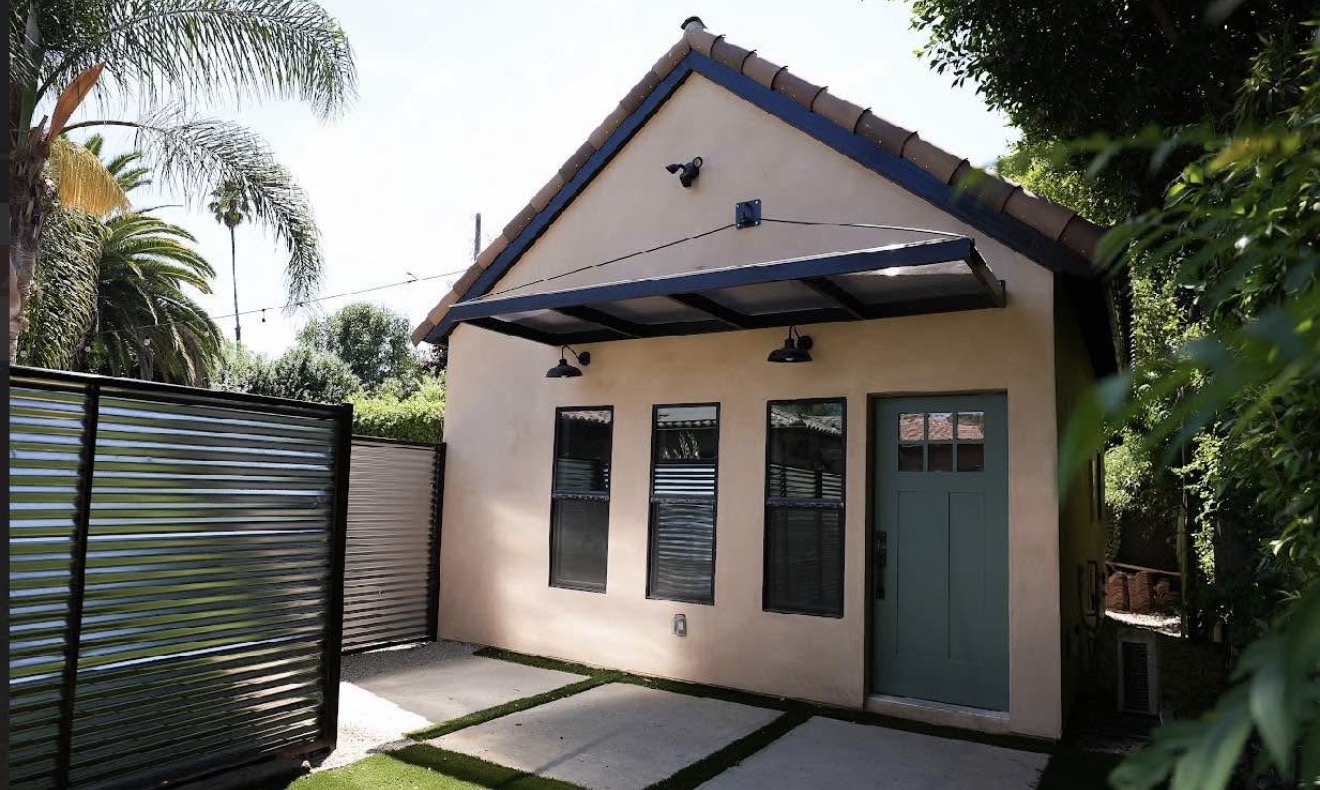 Completed ADU exterior — stucco finish, teal door, palm trees, stepping stone pathway
