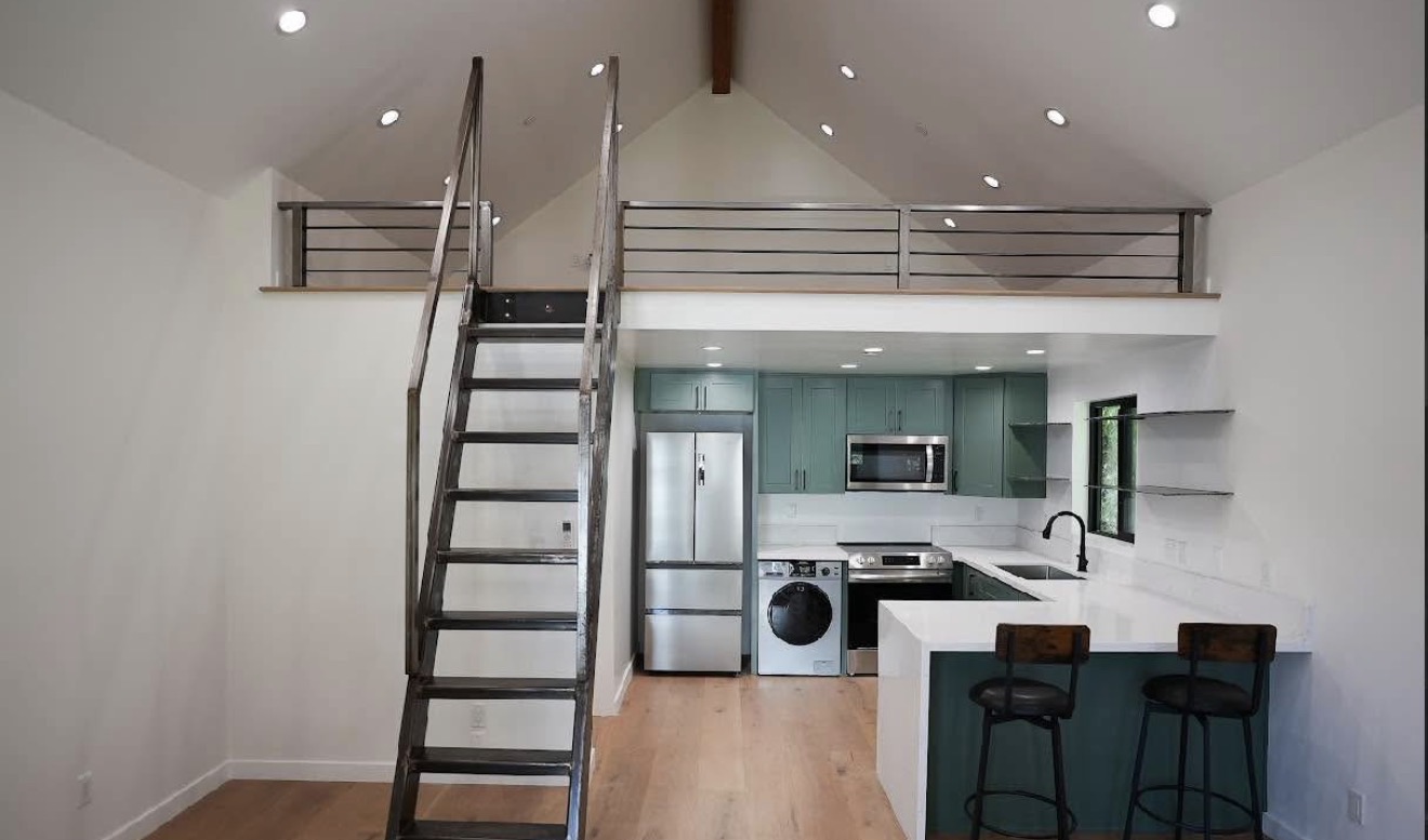 ADU loft interior — green kitchen, vaulted ceiling, metal staircase, bar seating