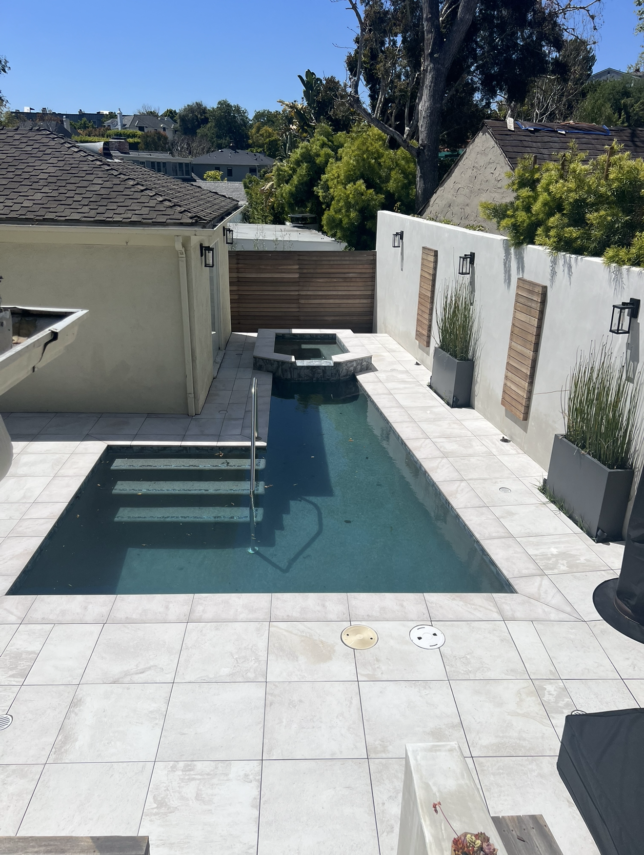 L-shape pool with porcelain tile deck in a small backyard
