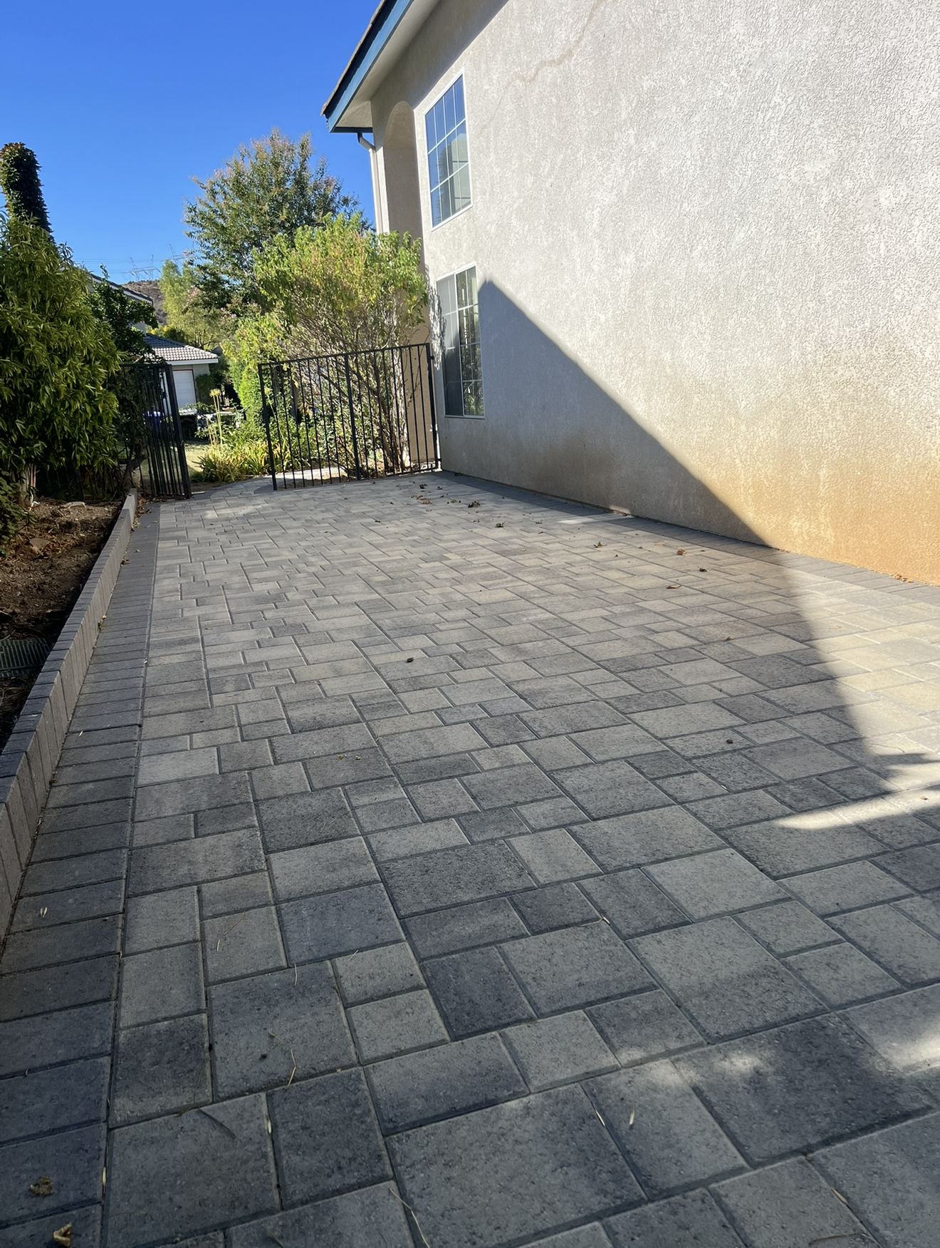 Finished narrow side-yard standard concrete paver walkway with gray pavers, a clean border and an iron gate