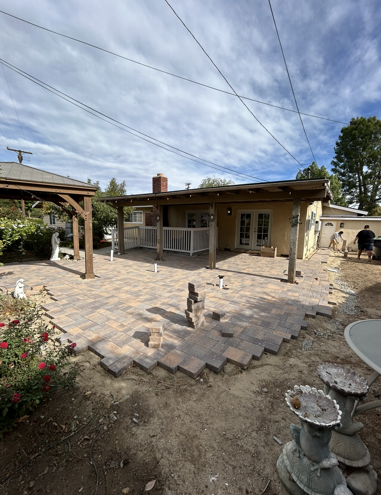 Large finished tan and brown standard concrete paver patio under a wood patio cover with a gazebo in the backyard